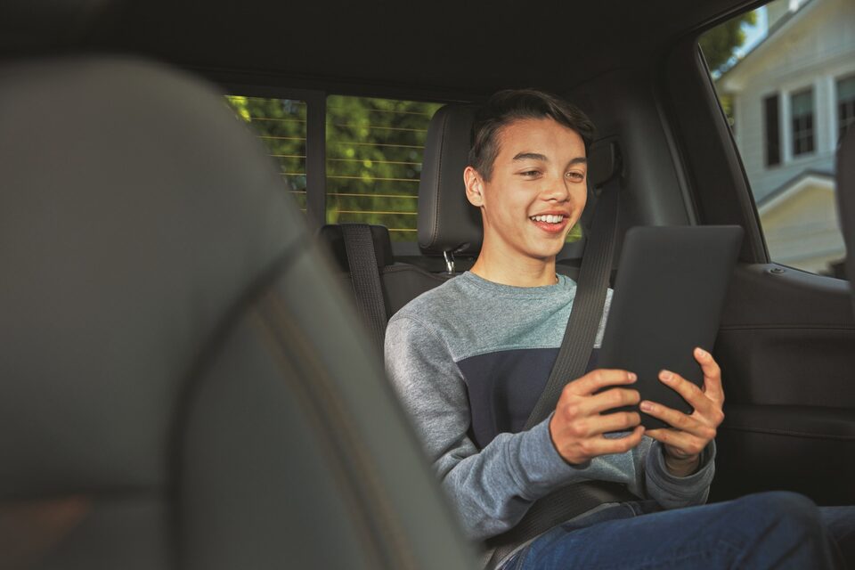 Smiling Child Using WarnerMedia Ride App on Compatible Device in GMC Vehicle