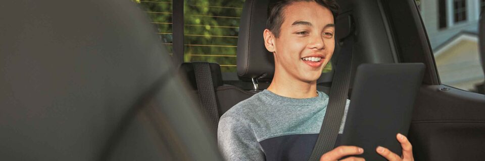 Smiling Child Using WarnerMedia Ride App on Compatible Device in GMC Vehicle