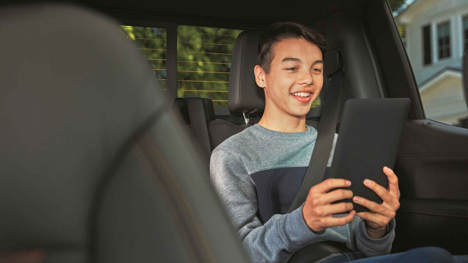 Smiling Child Using WarnerMedia Ride App on Compatible Device in GMC Vehicle