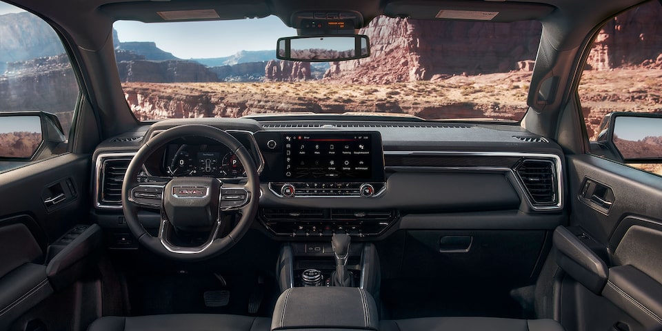 The Interior Dashboard and Steering Wheel of the GMC Canyon Truck with a Desert View Through the Windshield