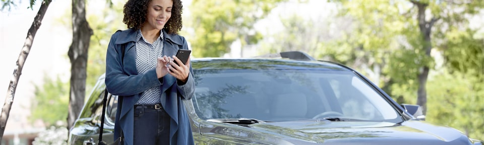 A Woman Standing In Front of her GMC Vehicle Using her MyGMC Mobile App