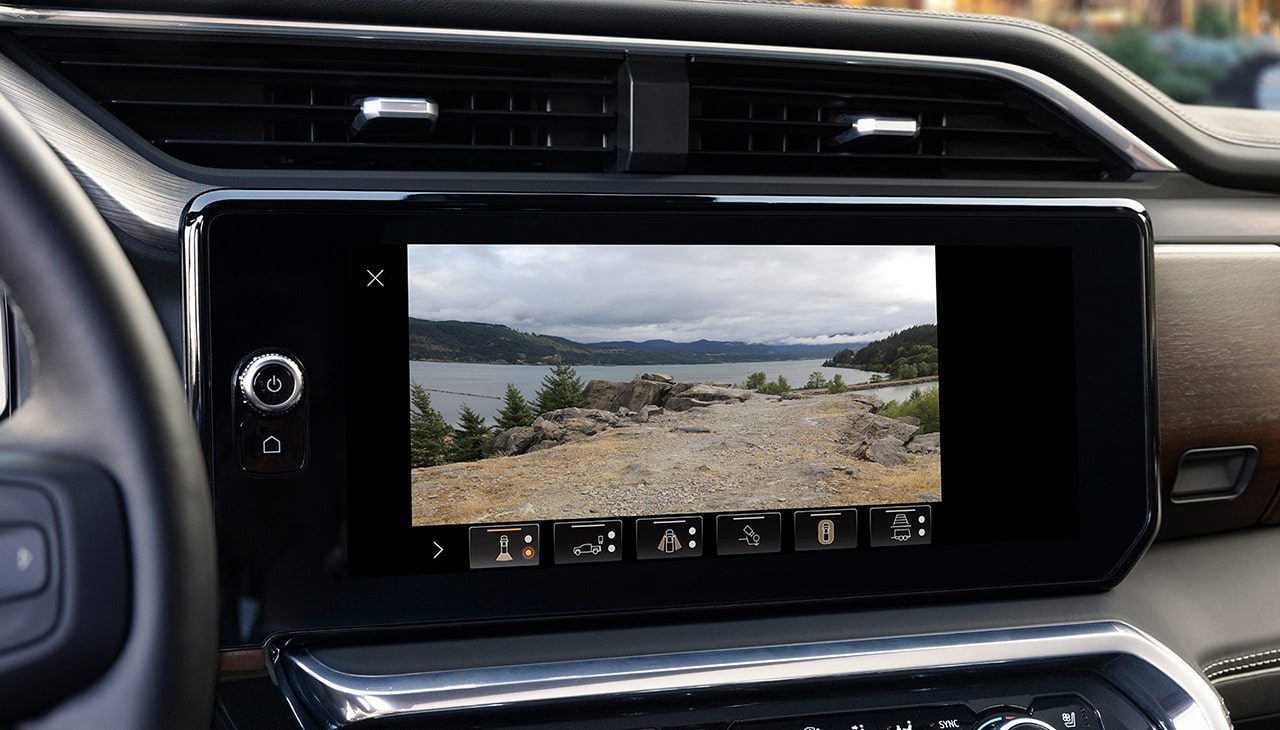 GMC Infotainment Screen Showing a High-Definition Rear Camera View of a Scenic Lake with Mountains and Trees