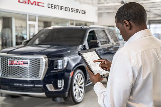 GMC Service Member Standing in Front of a GMC Vehicle Inspecting a Sheet of Vehicle Information