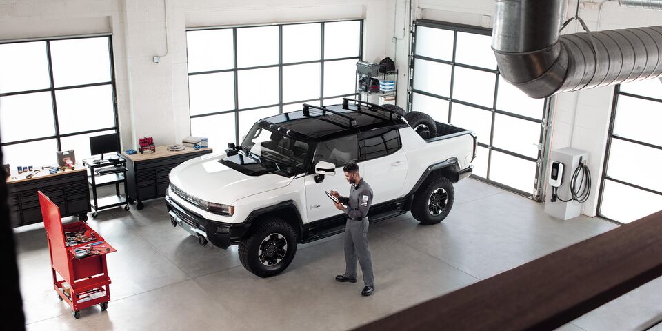 GMC Certified Service Technician Standing in a Service Bay Next to a GMC Hummer EV Truck