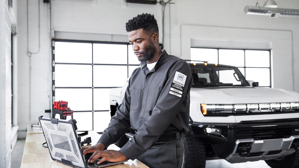 GMC Certified Technician Using a Laptop for Vehicle Diagnostics in a Well-Lit Garage