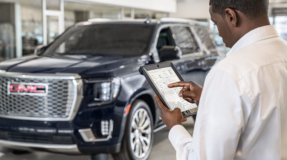 GMC Service Member Standing in Front of a GMC Vehicle Inspecting a Sheet of Vehicle Information