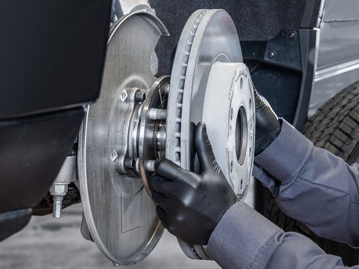 A Mechanics Hands Are Seen Placing a Metal Break Rotor for a Vehicle