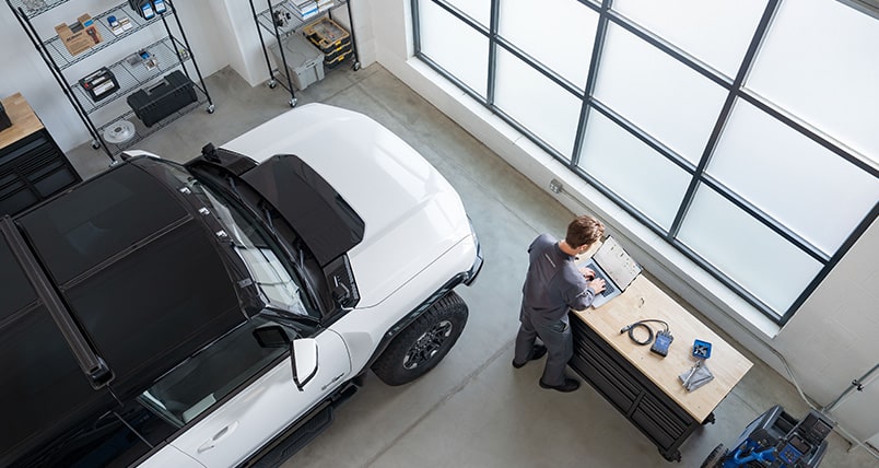 Birdseye View of a GMC Certified Service Technician Working on a Laptop Next to a Hummer EV