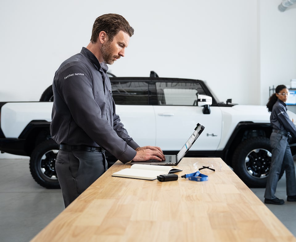 GMC Certified Service Technician Working on a Laptop with a GMC Hummer EV Truck Nearby