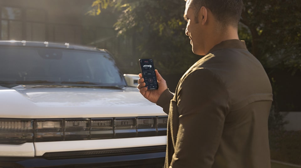 GMC Vehicle Owner Standing in Front of Their Hummer EV Checking The GMC EV App on Their Smartphone