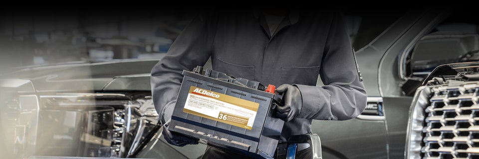 A Close-up View of a Service Technician Holding an ACDelco Battery While Standing in Front of a Vehicle.