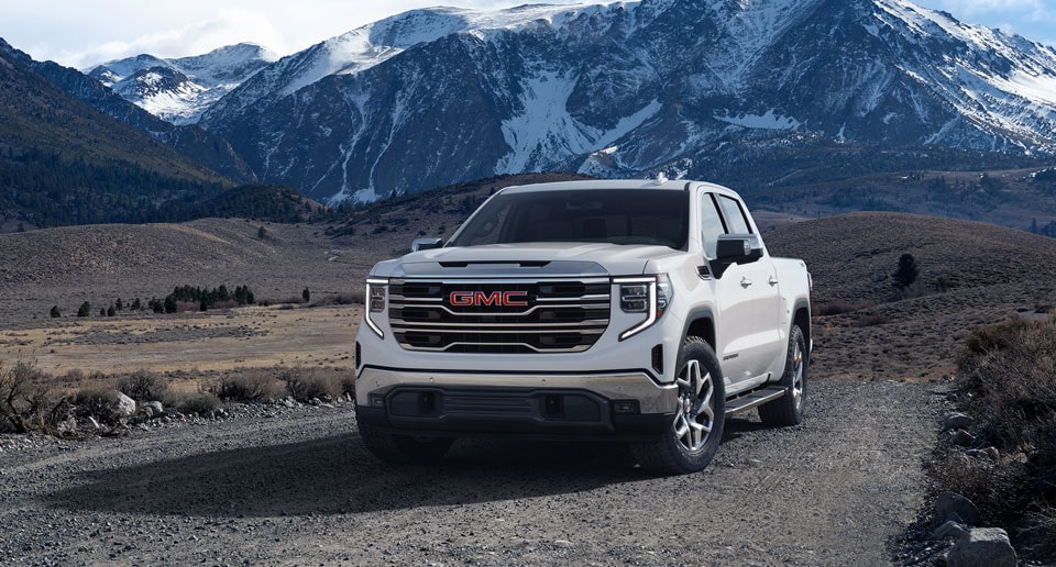 GMC Truck Driving on a Gravel Road with Snow Covered Mountains in Background