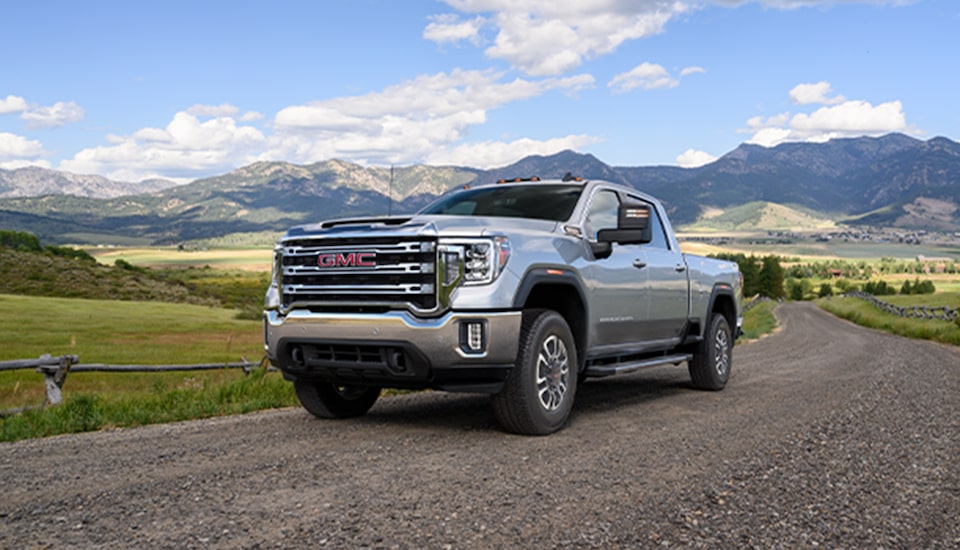 GMC Truck Driving on Gravel Road with Snow Covered Mountains in Background