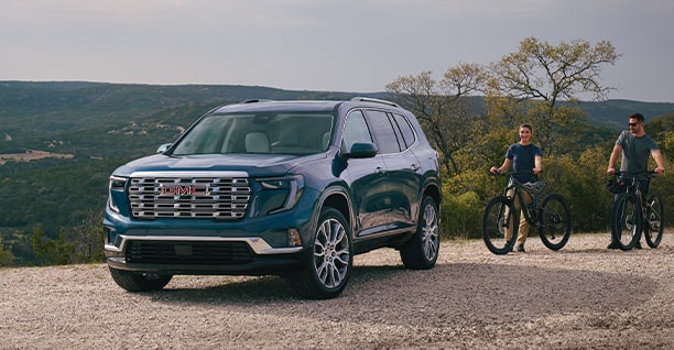 A Blue GMC SUV Outdoors with Two Bicyclists Nearby