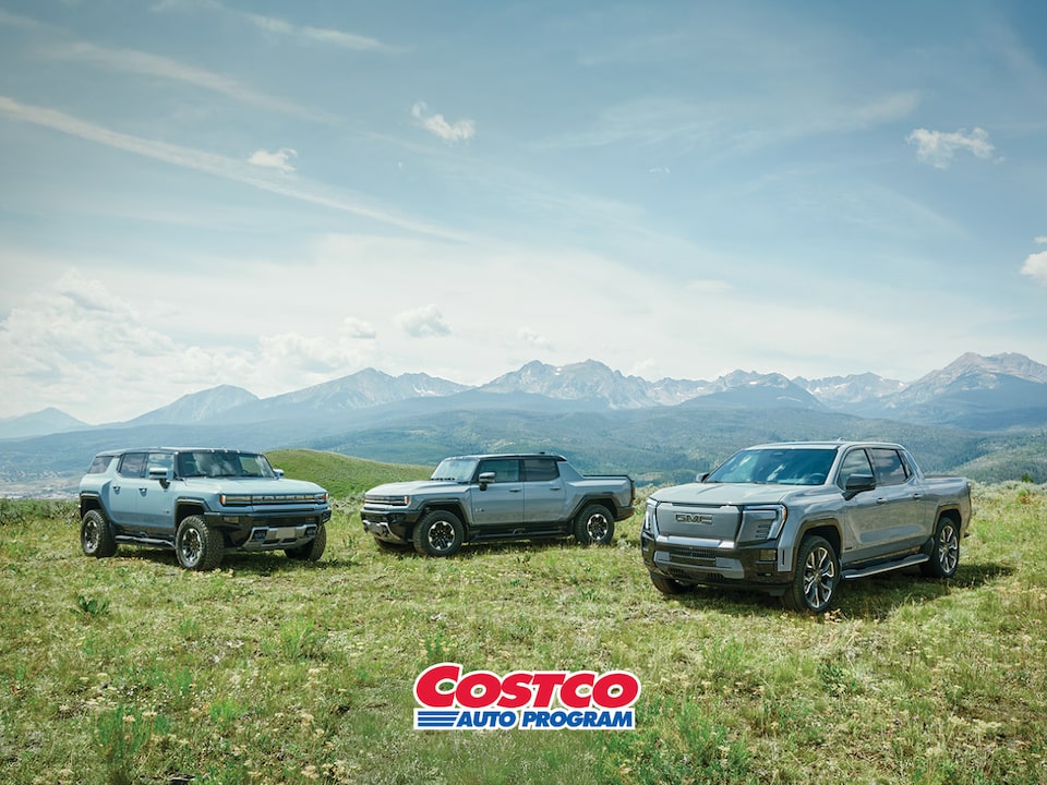 The GMC EV Lineup Parked in a Green Valley with Mountains in the Distance with Text Overlay: GMC COSTCO AUTO PROGRAM