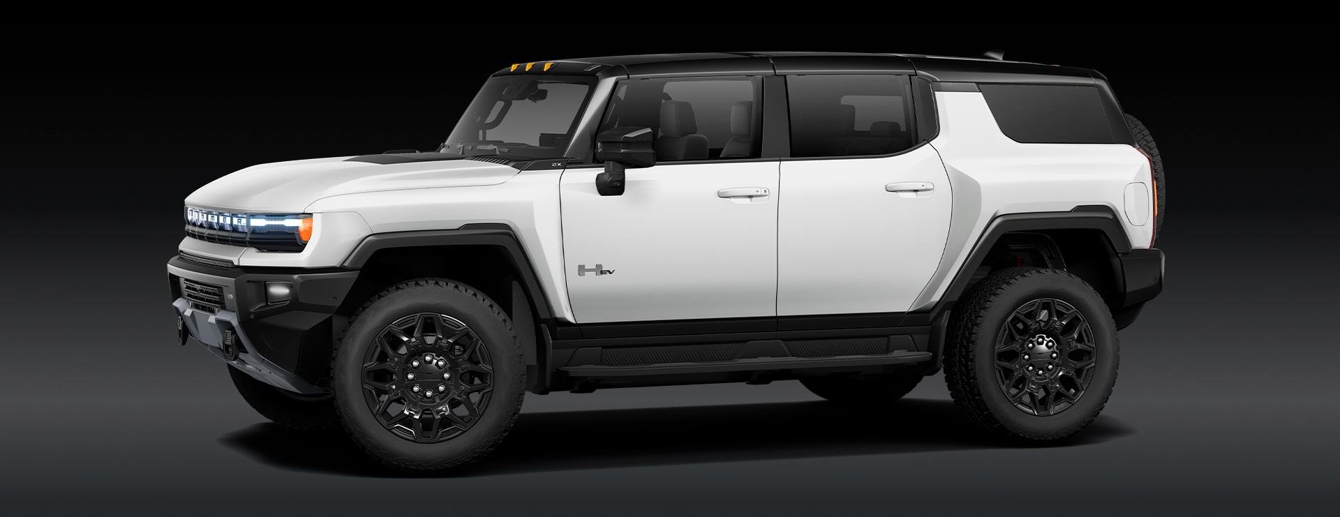 A White GMC HUMMER EV SUV Is Parked From a Front Three-Quarters Angle Against a Dark Background