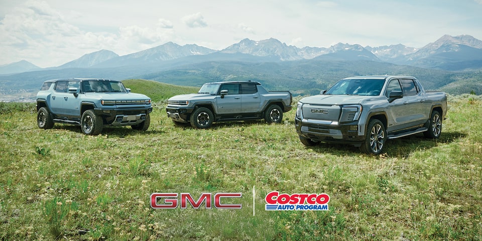 The GMC EV Lineup Parked in a Green Valley with Mountains Surrounded by Blue Skies in the Distance