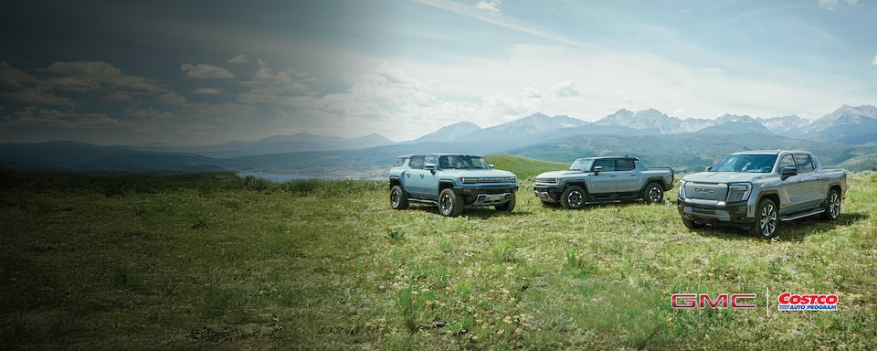 The GMC EV Lineup Parked in a Green Valley with Mountains Surrounded by Blue Skies in the Distance