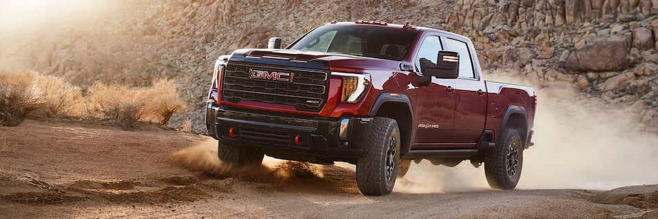 A GMC Sierra 1500 AT4 Truck Kicking Up Dust While Driving on a Gravel Path Next to Mountains During Sunset