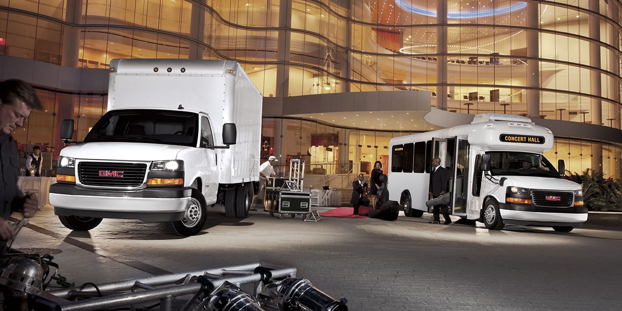 Two GMC Commercial Savana Cutaway Vans Parked in Front of a Large Building