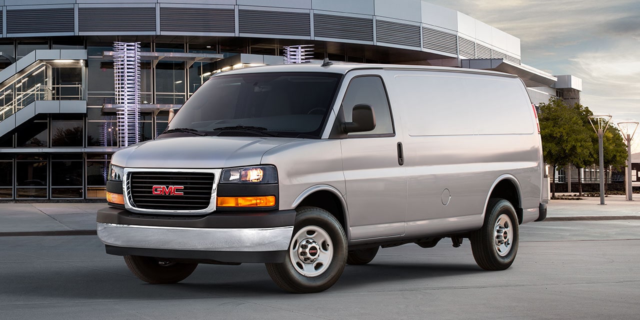 Front Three-Quarters View of the GMC Commercial Savana Cargo Van Parked in Front of a Large Building