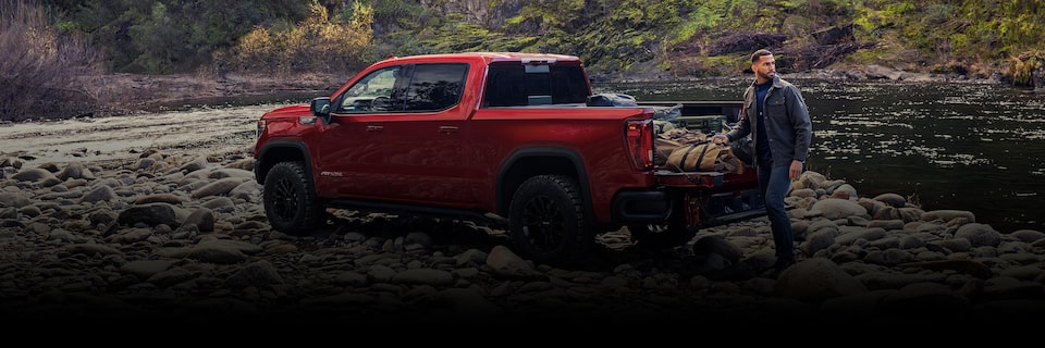 A Red GMC Pickup Truck Parked Off-Road with a Man Pulling Supplies from the Bed