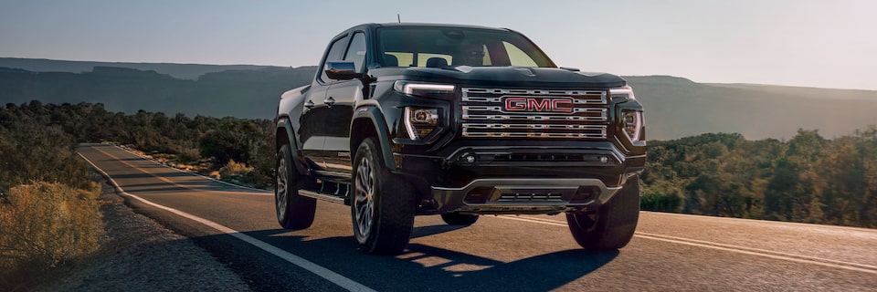 Front Three-Quarters View of a GMC Canyon Denali Truck Driving on a Open Road During Sunset