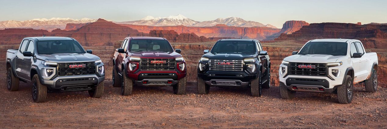2024 GMC Red Cayon, Gray Cayon AT4, White Denali and Black AT4X  trucks parked in the desert