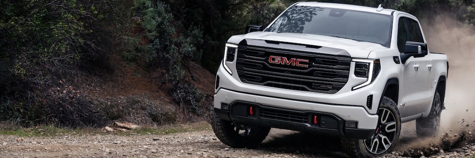Summit White GMC Sierra Driving Off-Road Kicking Up Dust With Trees