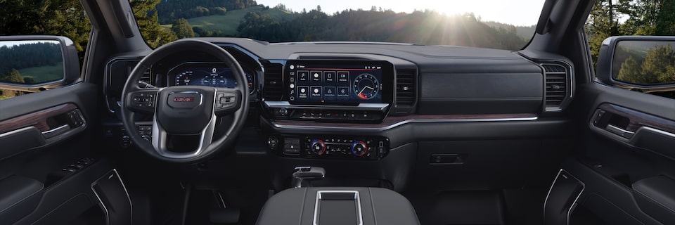 Steering Wheel, Dashboard, and Infotainment System on the GMC Sierra Parked Off-Road with Sun and Trees