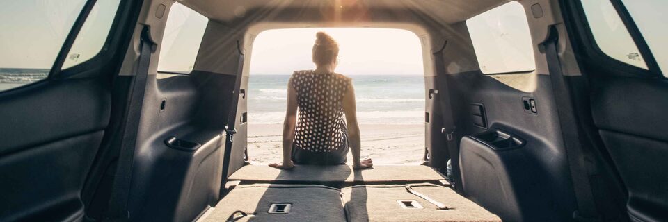 Women With Her Back to Camera Sitting in the Trunk of the GMC Acadia Parked On Beach With Sunset
