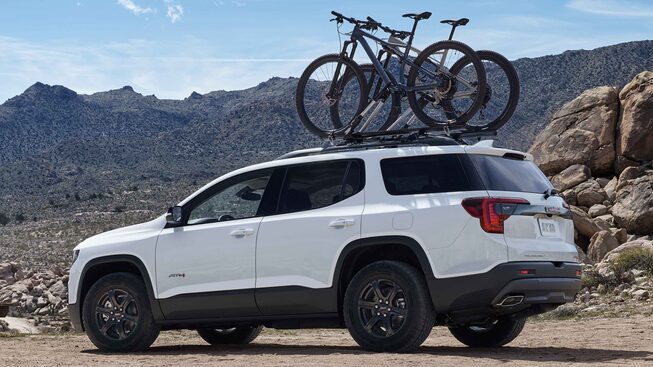The Summit White GMC Acadia AT4 Driving Off-Road With Bikes on the Rack