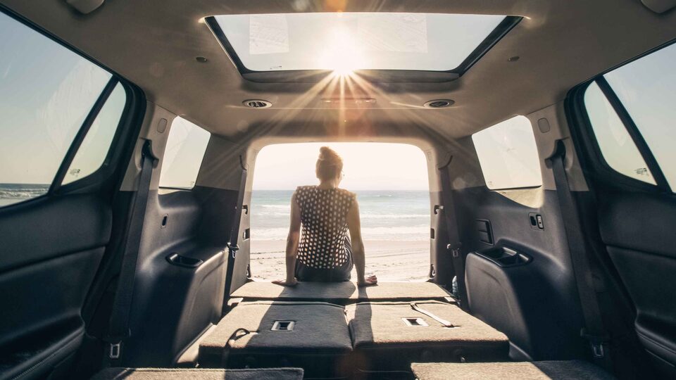 Women Sitting in the Open Trunk of her GMC Acadia Parked on Beach With Sunset