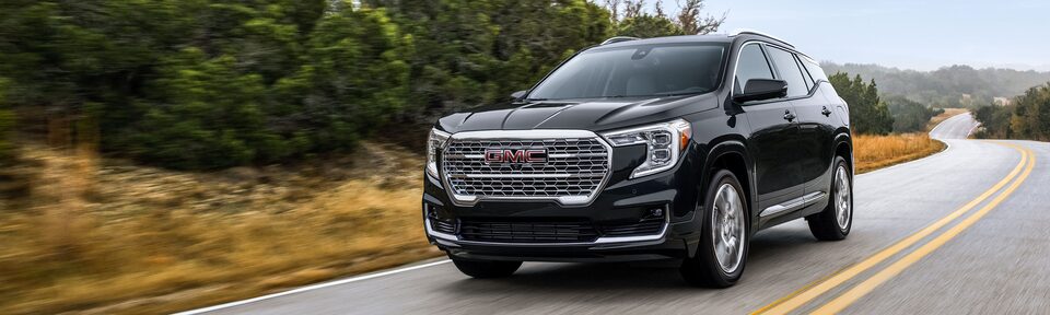 Ebony Twilight Metallic GMC Terrain Driving On-Road With Grass and Trees