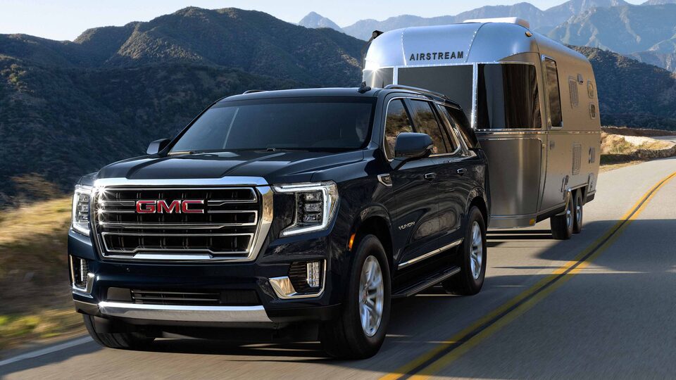Dark Blue Metallic Yukon Towing a Airstream Trailer On-Road With Hills and Clear Sky