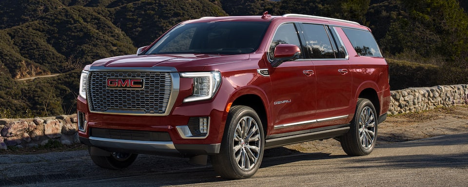 Red Yukon Parked On-Road Next to Stone Wall With Hills