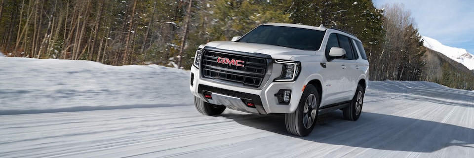 White GMC Yukon AT4 Off-Road Truck Driving on Snow with Woods