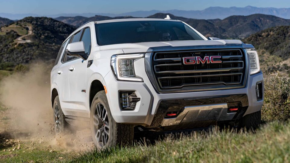 White GMC Yukon AT4 Off-Road SUV Driving Uphill in a Valley with Dirt Kicked Up