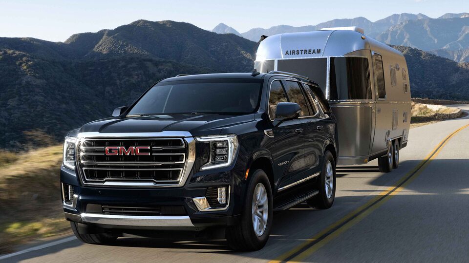 Black Yukon SLT Large SUV Driving on the Road pulling a Airstream Trailer