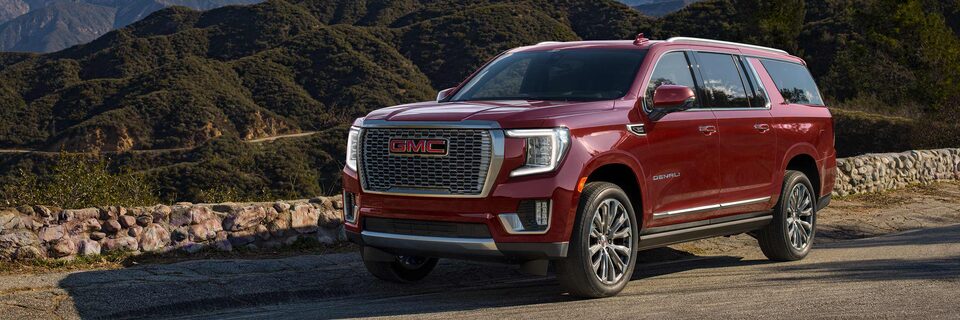 Red GMC Yukon Parked on Road With Small Wall and Hills