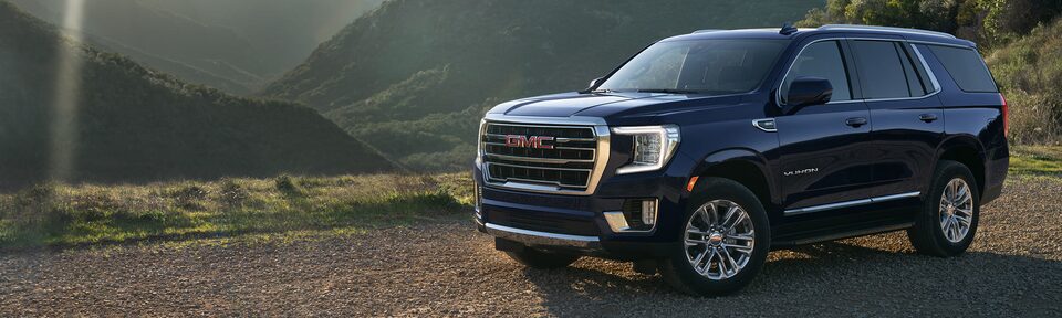 Dark Blue Metallic Yukon Parked Off-Road On Rocks With Hills and Trees