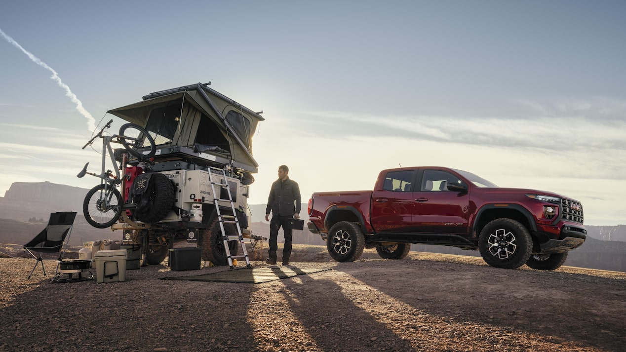 Red GMC Canyon AT4X parked on a hill with a man un packing the midsize roof camper.