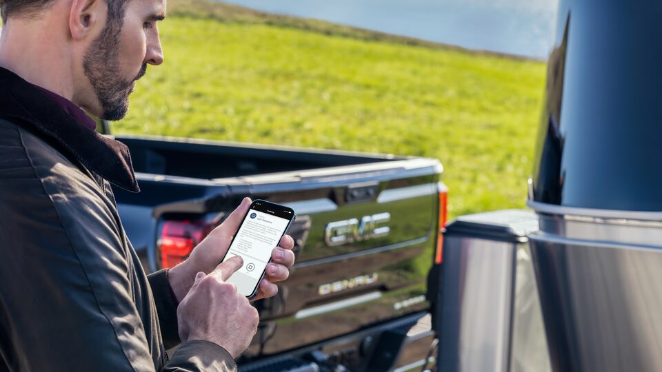 A Man Using the MY GMC App on his Phone next to his GMC Vehicle
