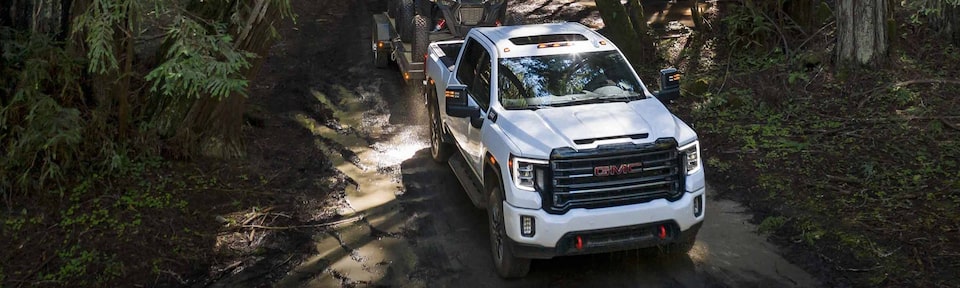 The Powerful Summit White GMC Sierra HD AT4 Driving Off-Road Through Trees and Mud