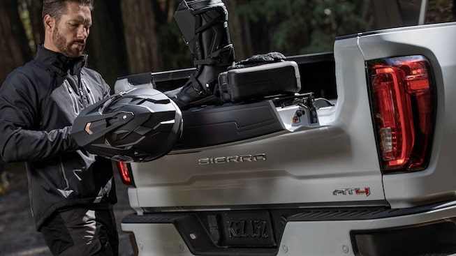 Man Holding Helmet Loading Off-Road Equipment into the bed of the GMC Sierra HD AT4