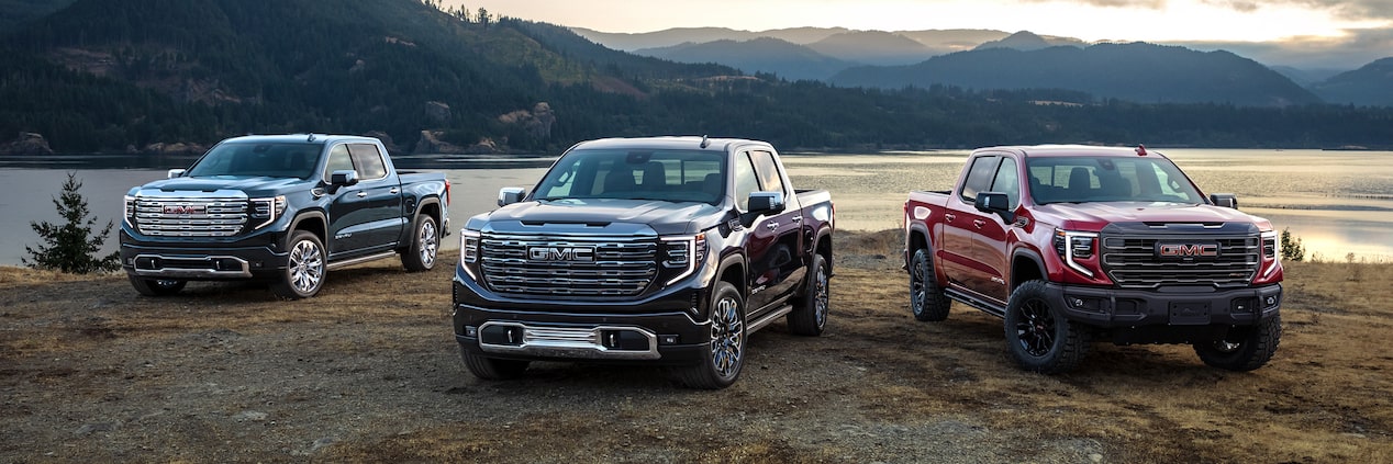 Three 2023 GMC Sierra 1500 models lined up with a mountains and a body of water in the background