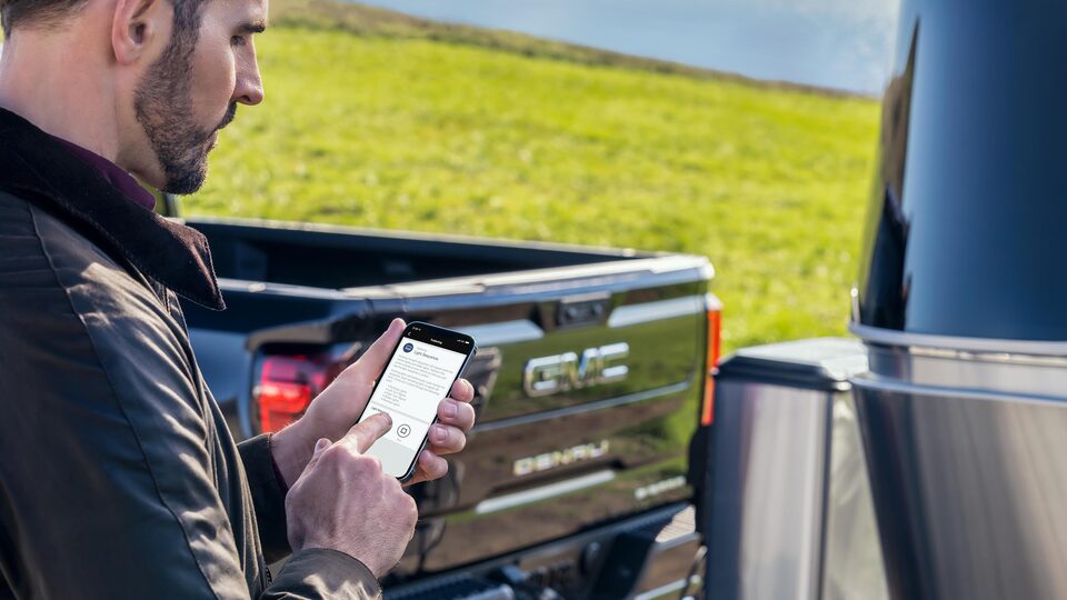 A Man Utilizing the GMC Mobile App while next to the GMC Sierra LD