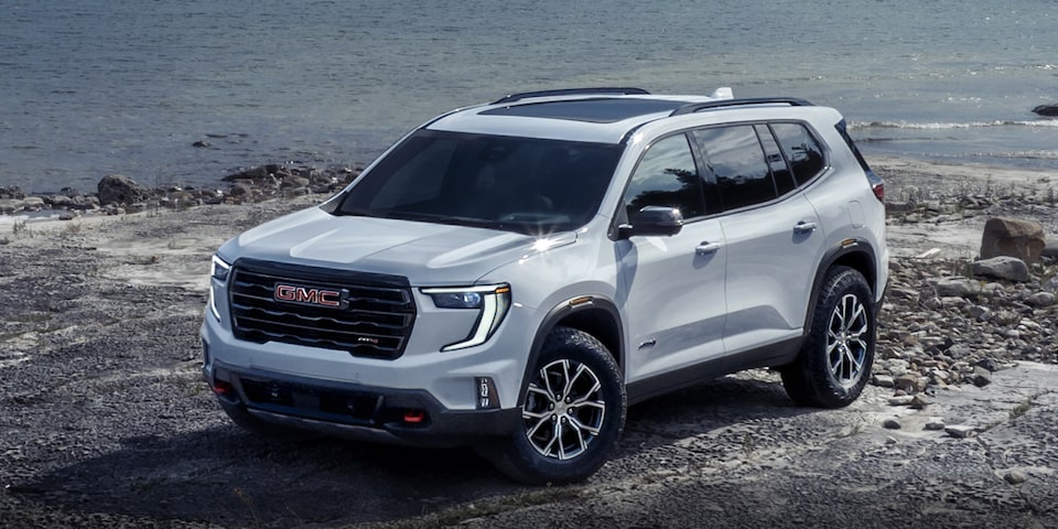 Front Three-Quarters View of a 2024 GMC Acadia AT4 SUV Parked in Front of a Lake