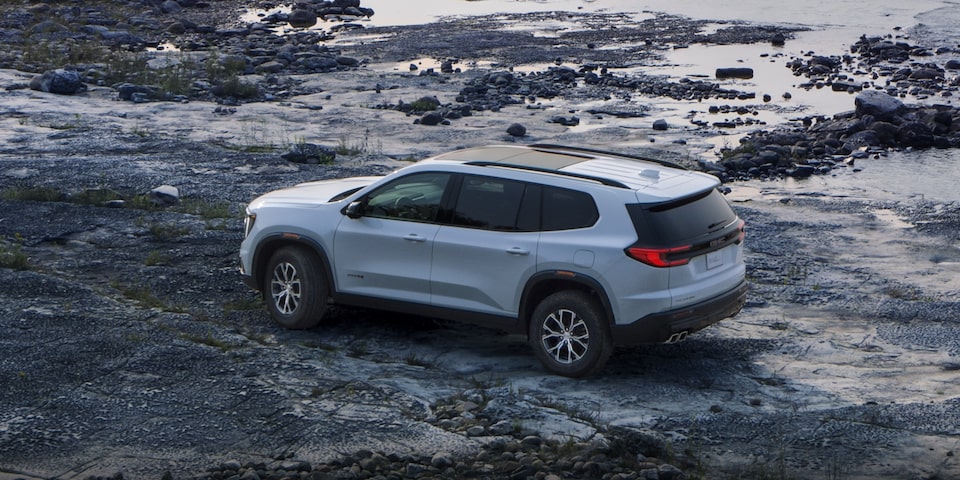 Wide Rear Three-Quarters View of a 2024 GMC Acadia AT4 Parked on a Rocky Path