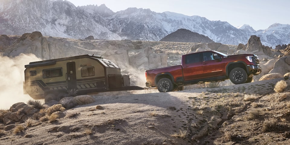 The Sierra HD AT4 Driving Quickly Through Uneven Rocky Terrain as it Tows a Camper with Ease